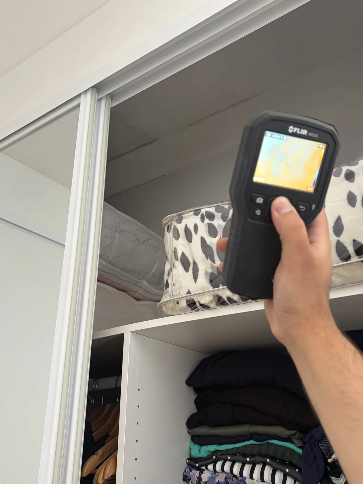 Ibrahim holding a FLIR thermal camera up to a wardrobe interior during a termite inspection