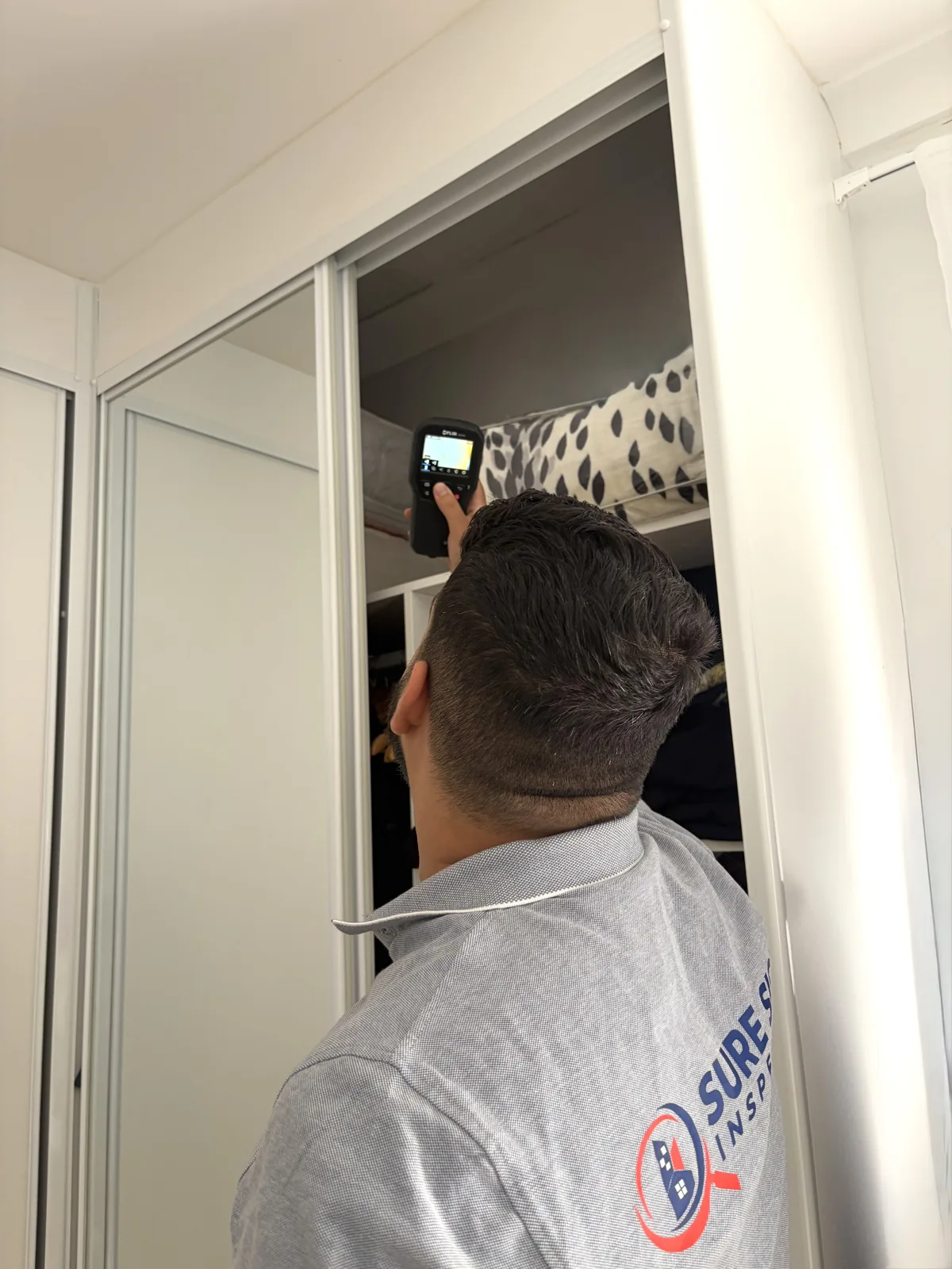 Ibrahim scanning the top of a built-in wardrobe with a thermal camera